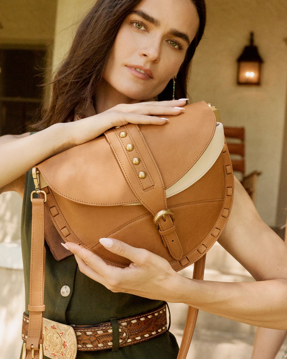 Woman holding a brown leather saddle bag outdoors