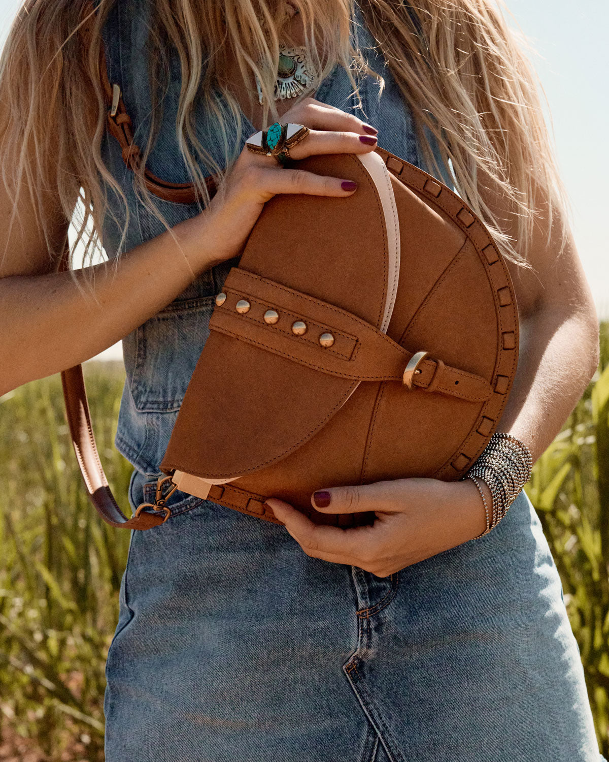 Person holding a brown leather bag in a field