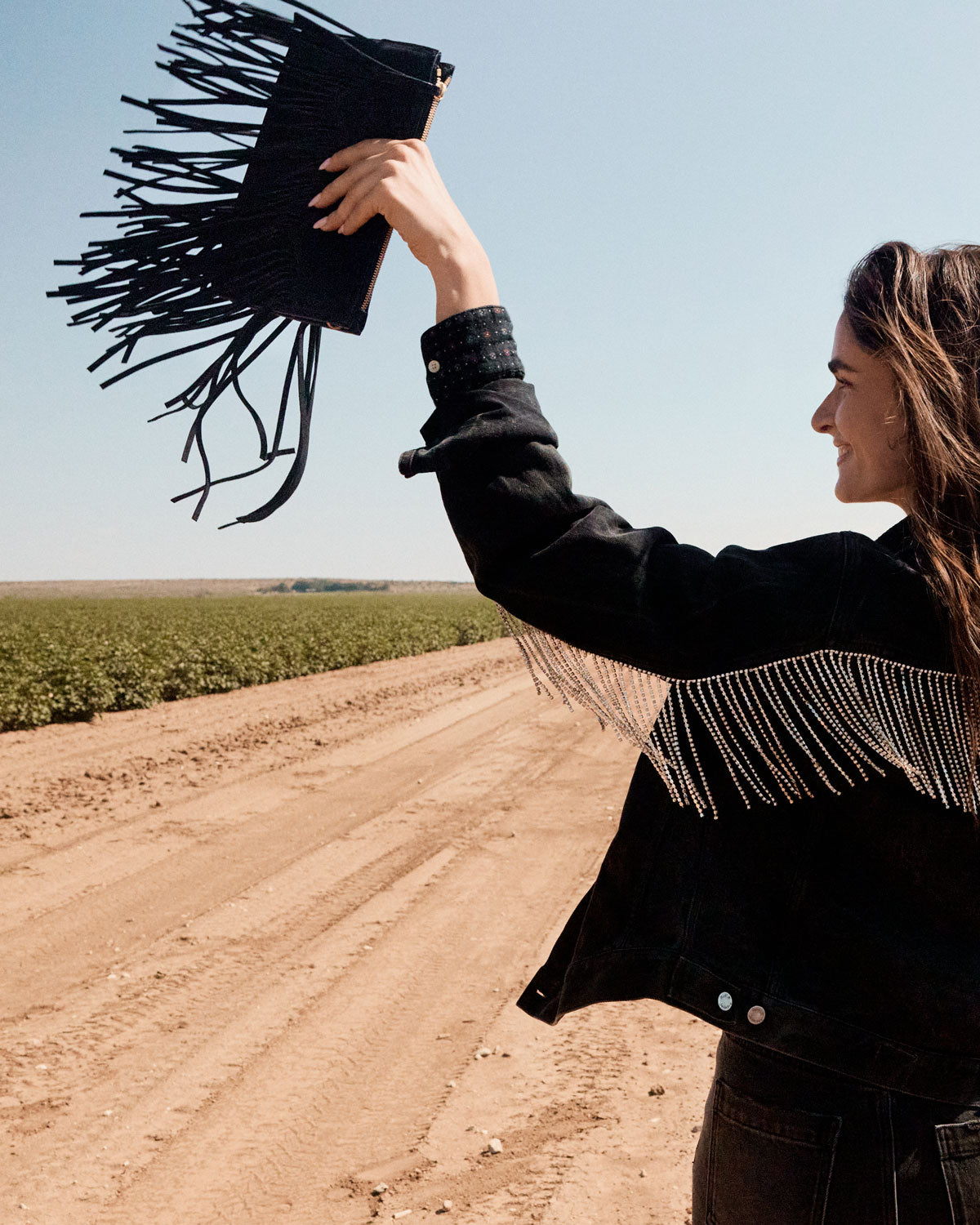 Person holding a black fringe bag in an open field