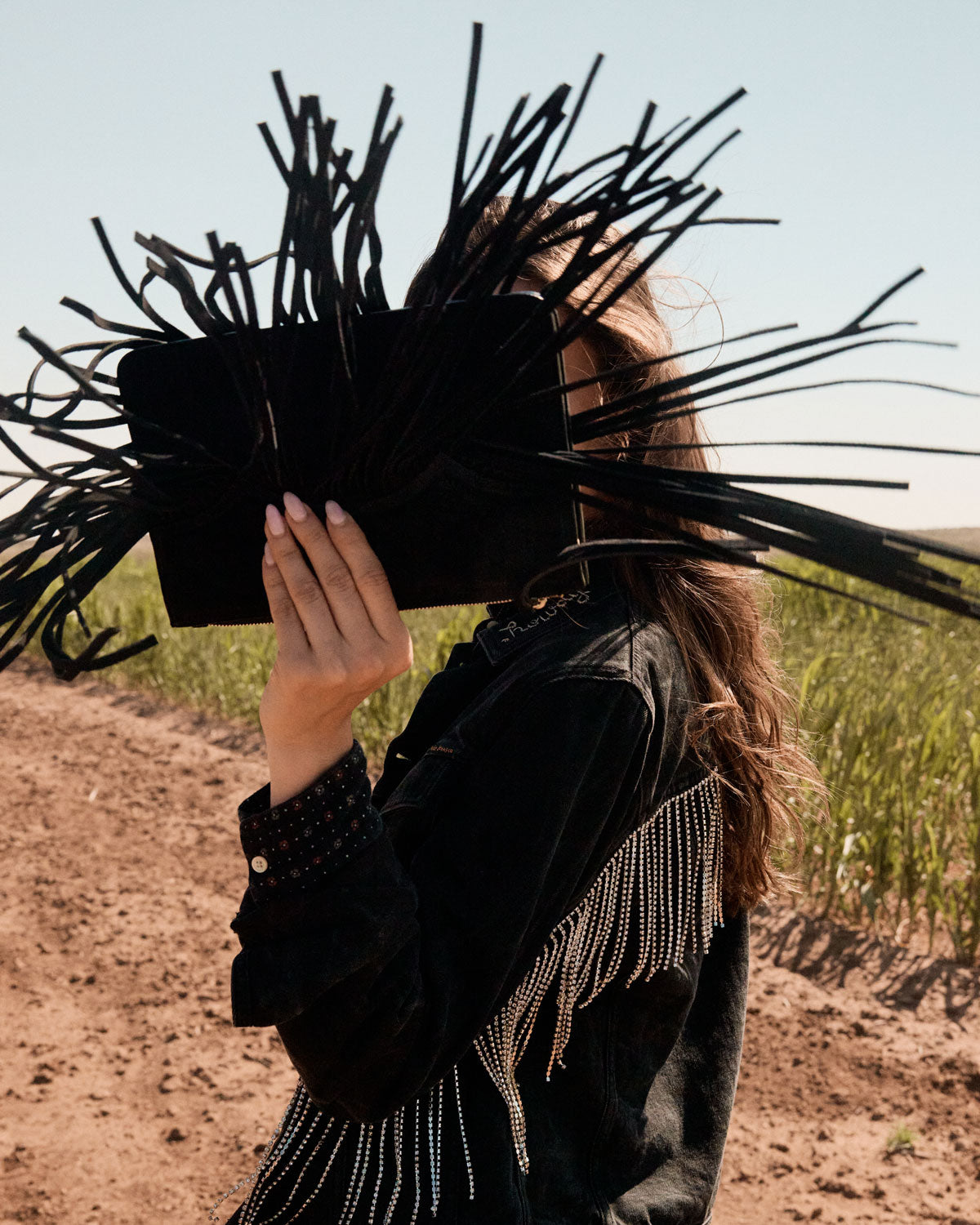 Person holding a black clutch with long black sticks in a field