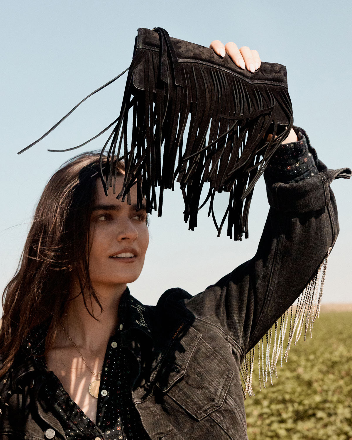 Woman holding a black fringe handbag against a clear blue sky