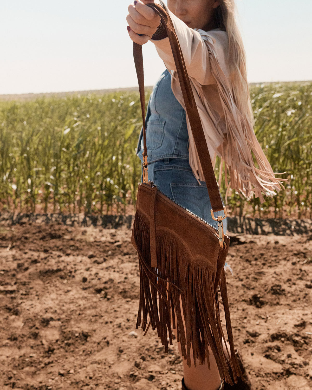 Person holding a brown fringe handbag in a field