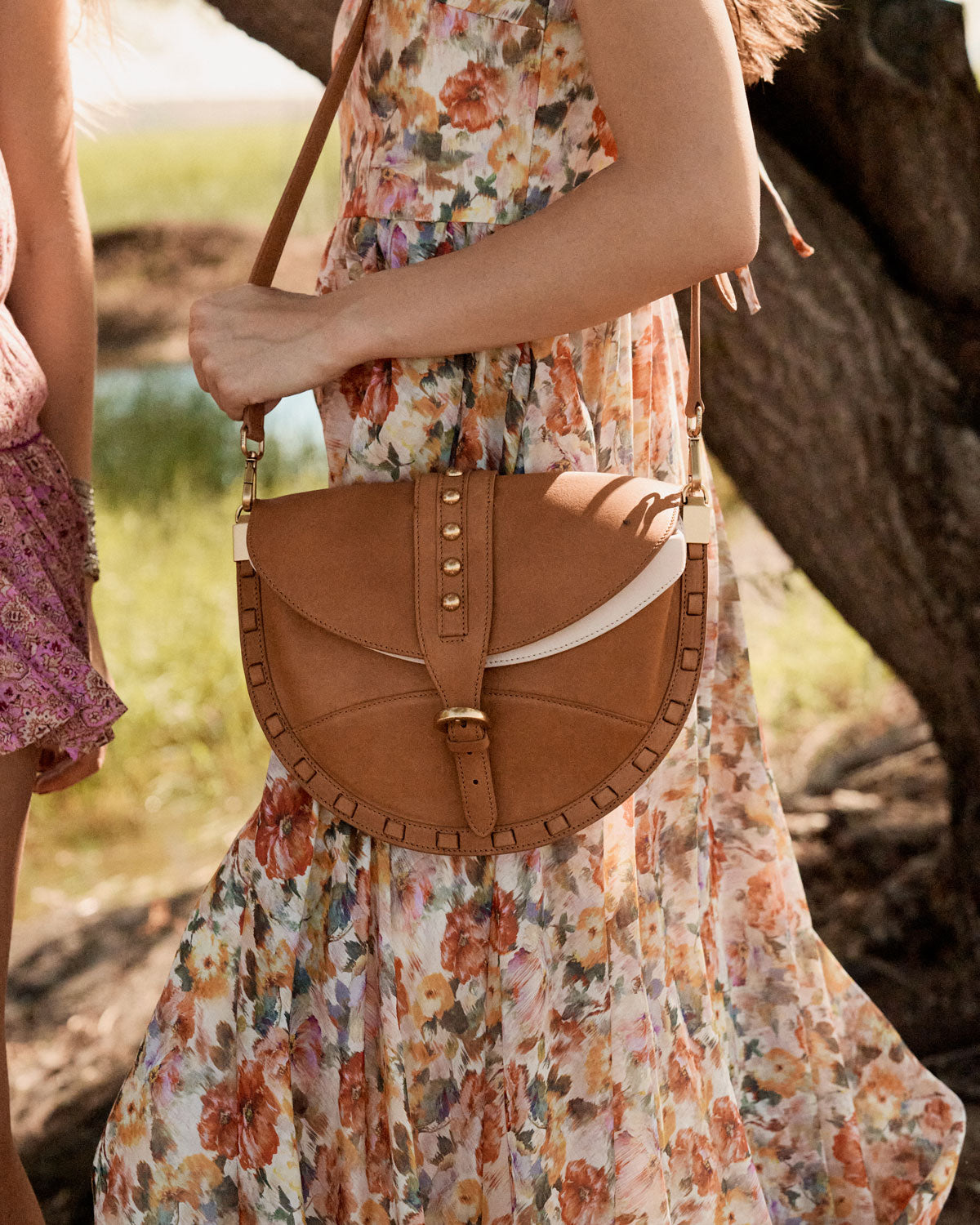Person wearing a floral dress holding a brown leather handbag outdoors.