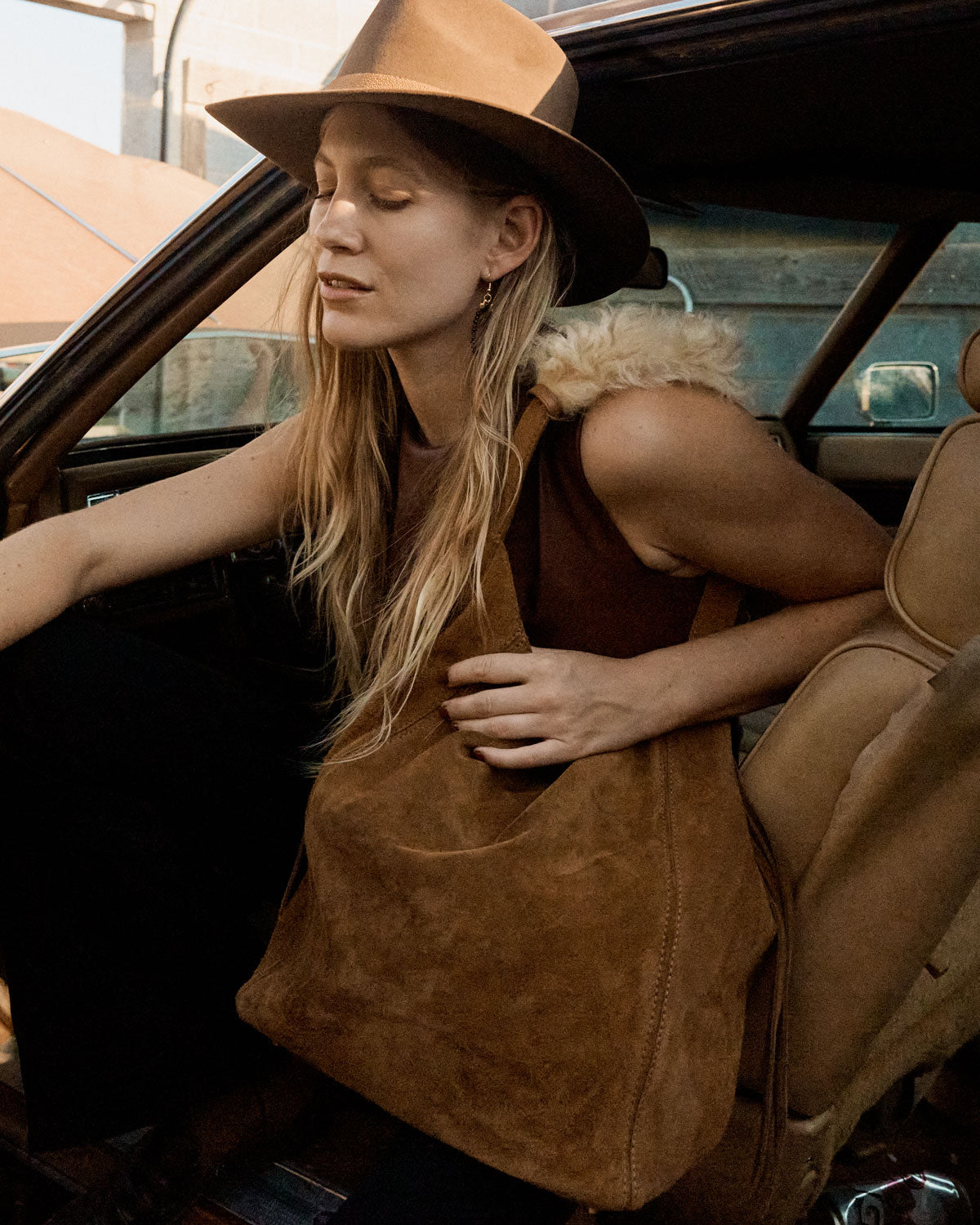 Woman in a car wearing a brown hat and bag, with a vintage car interior.