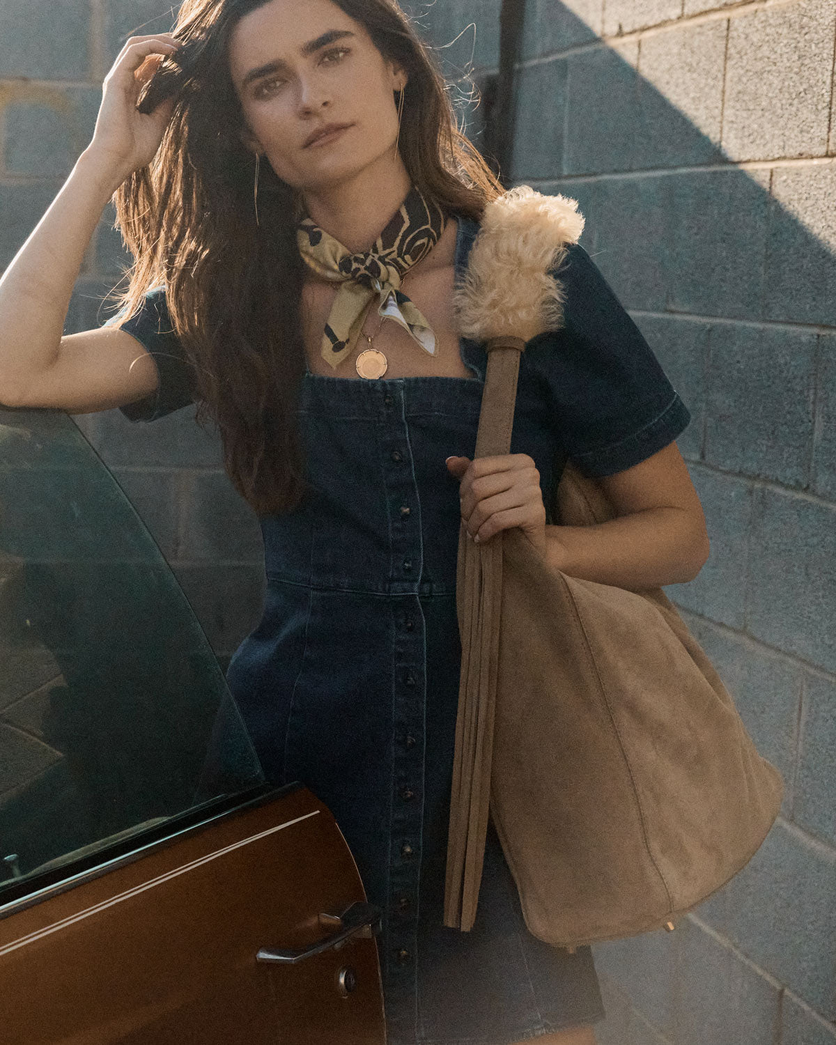Woman with long hair holding a handbagagainst a brick wall.