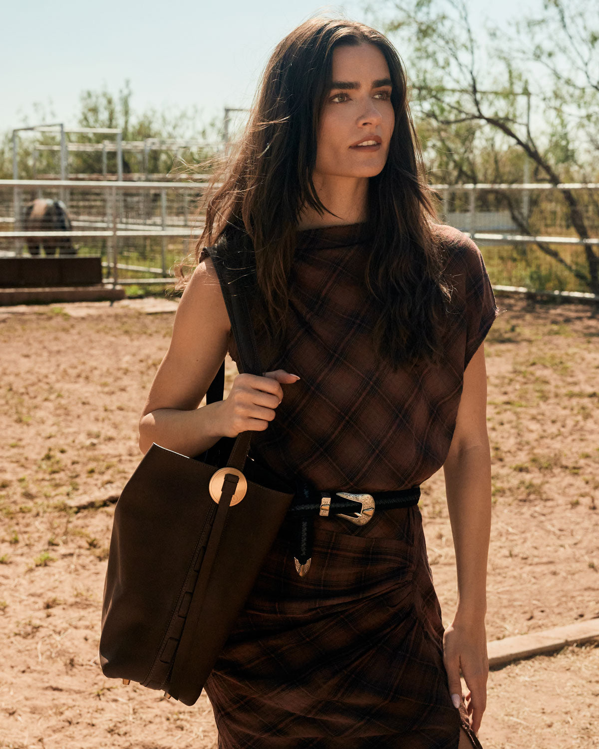 Woman in a brown outfit holding a large bag outdoors.