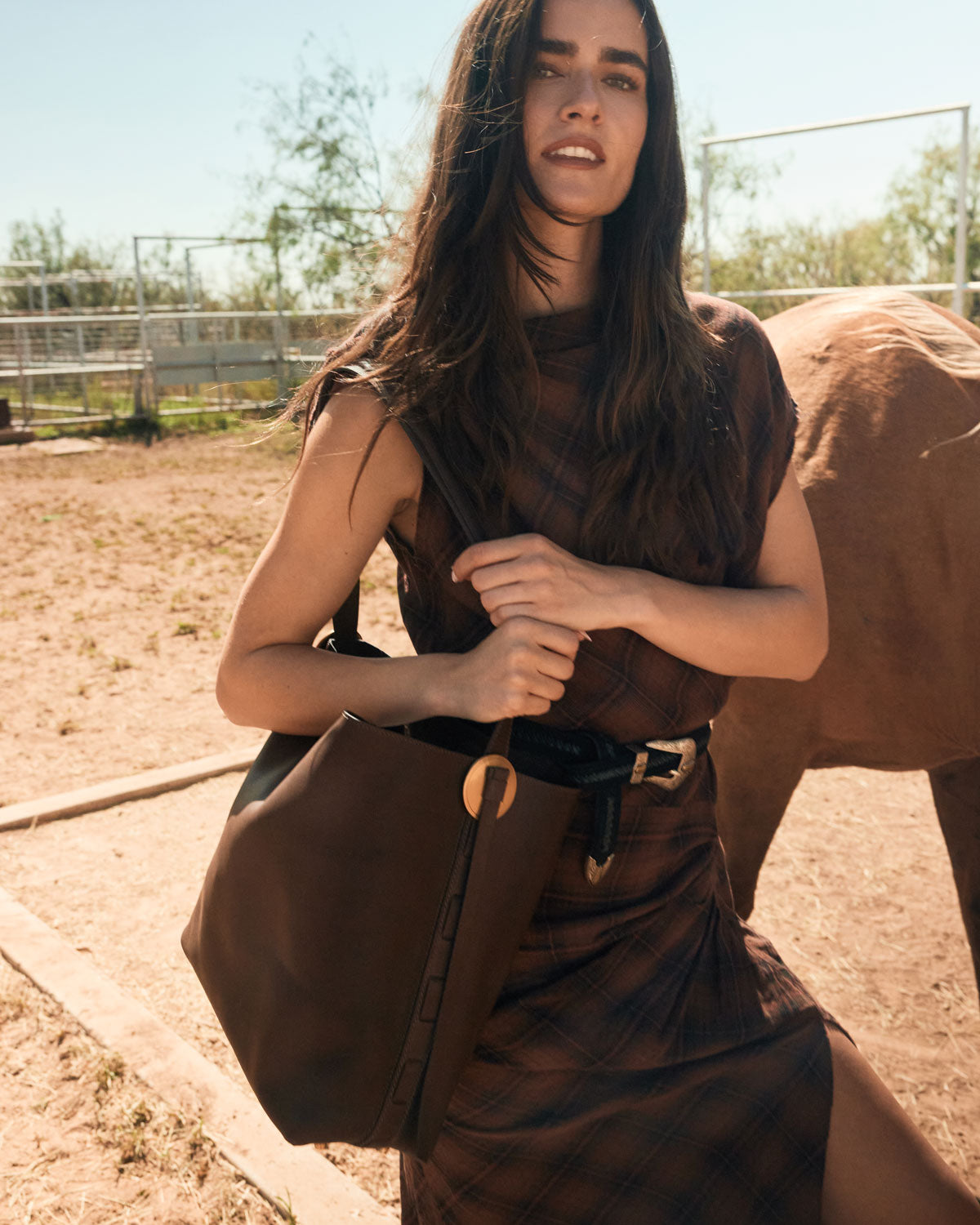 Woman holding a brown leather bag with a horse in the background