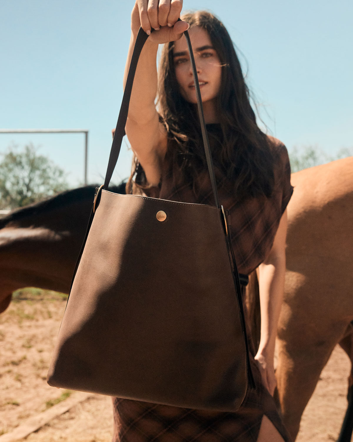 Woman holding a brown leather tote bag with a horse in the background
