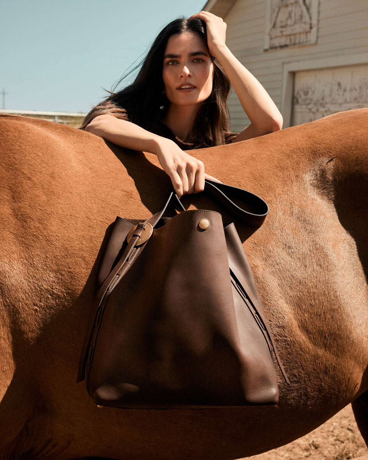 Woman holding a brown leather bag on a horse in an outdoor setting