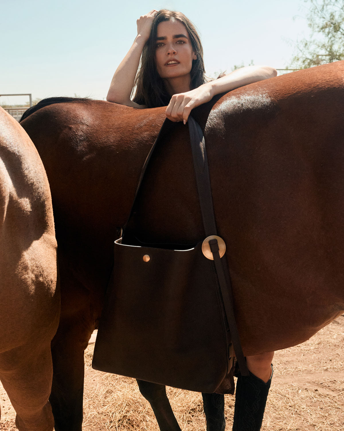 Woman standing next to a horse wearing a brown leather bag with a wooden buckle.