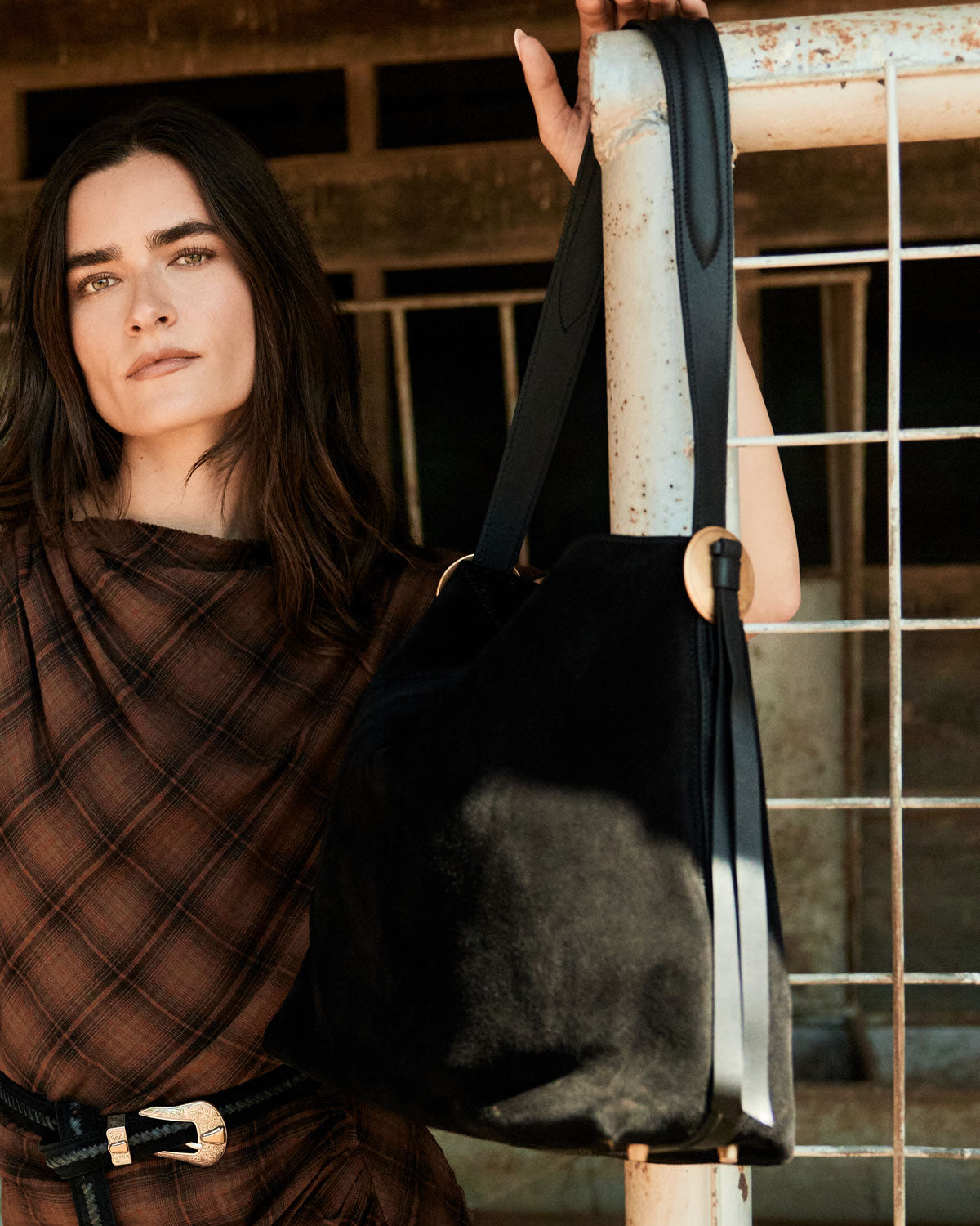 Woman holding a black bag with a metal handle against a rustic background