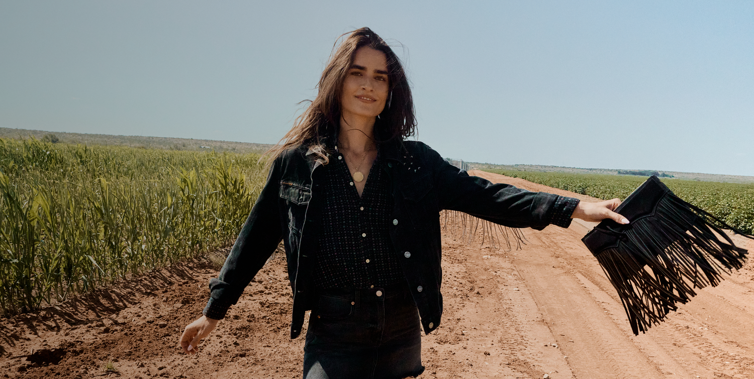 Woman holding a black fringed bag in a field