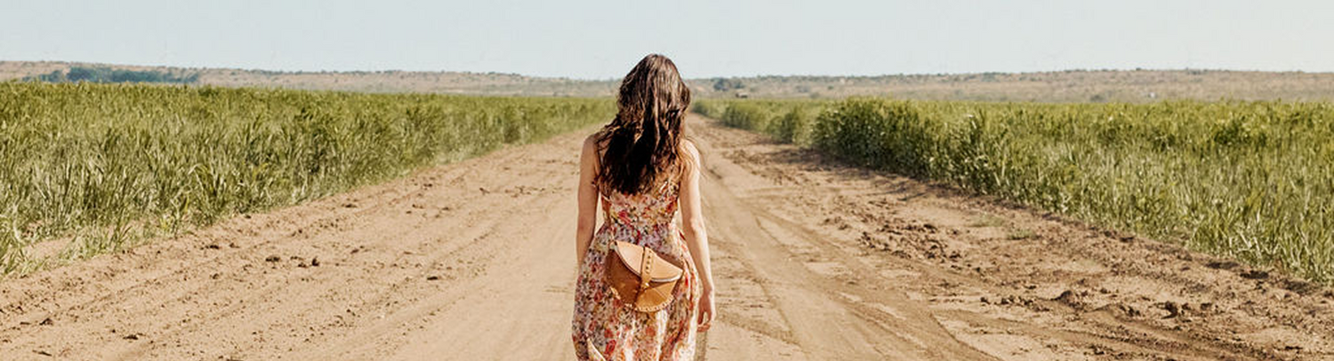 Woman walking down a dirt road in a field with a clear sky