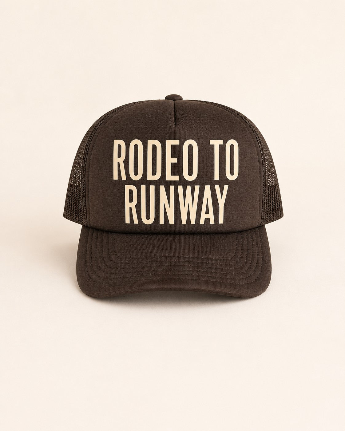 Brown trucker hat with 'Rodeo to Runway' text on a light background
