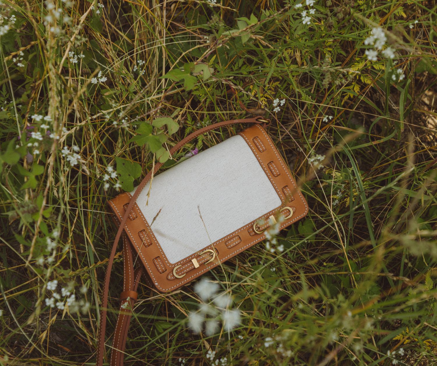 Close-up of a bag with light linen panel and brown leather straps on a natural background