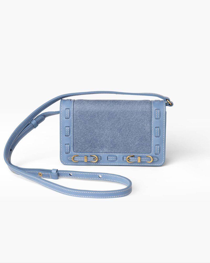 Blue denim crossbody bag with brass hardware on a white background