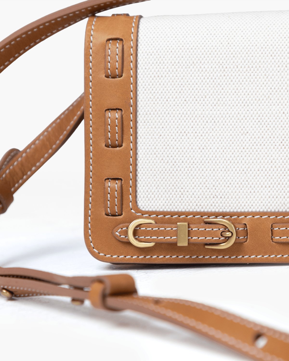 Close-up of a bag with linen panel brown leather strap and stitching details on a white background