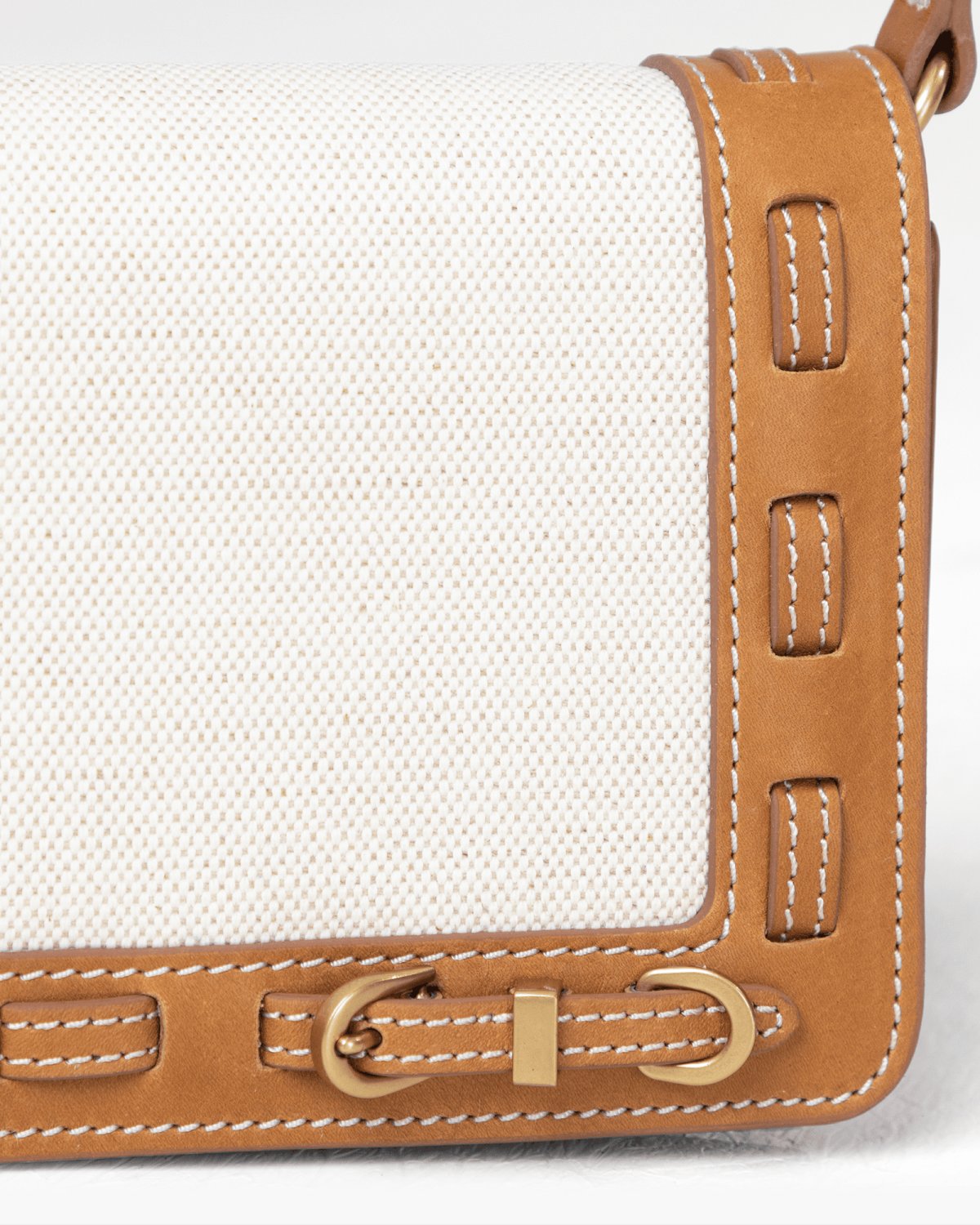 Close-up of a bag with a light linen panel brown leather trim and brass hardware on a light gray background