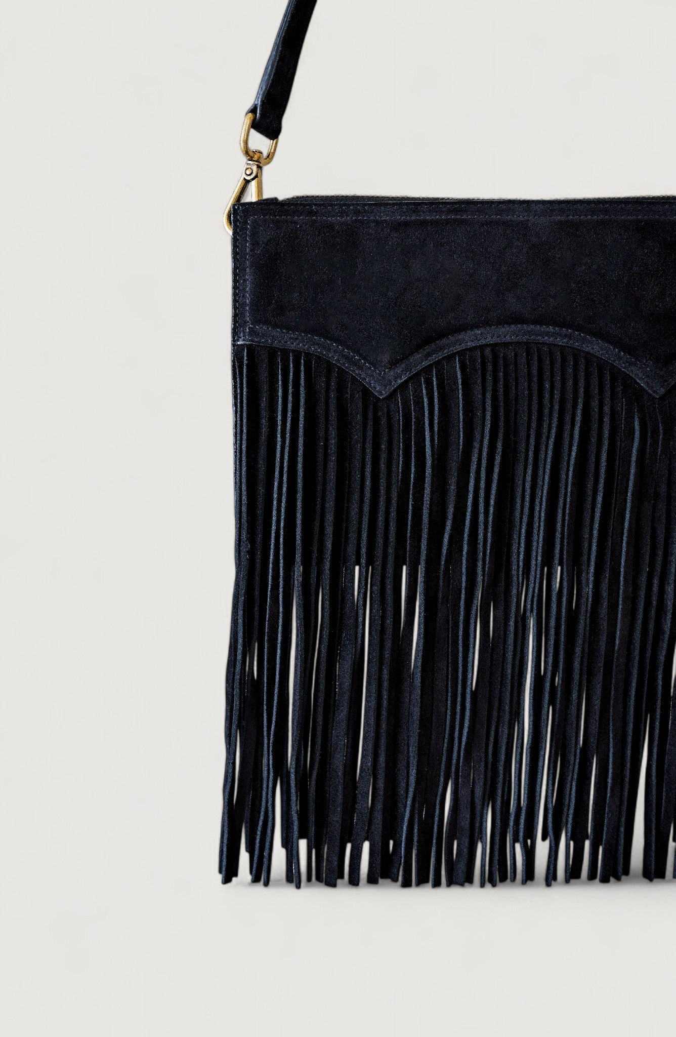 Black suede handbag with fringe details on a light gray background