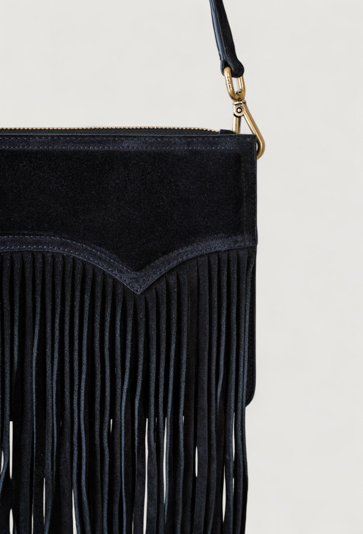 Black fringe handbag with a brass zipper on a light gray background