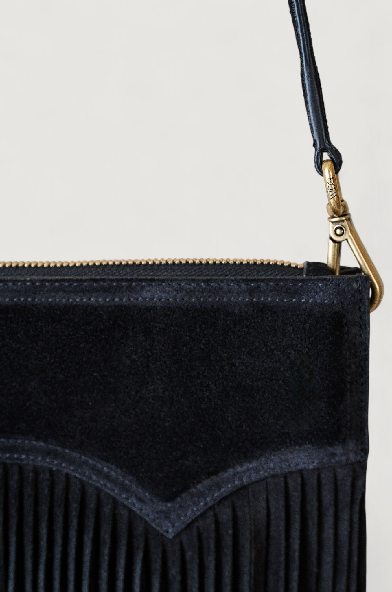 Black suede handbag with fringe detail on a light beige background