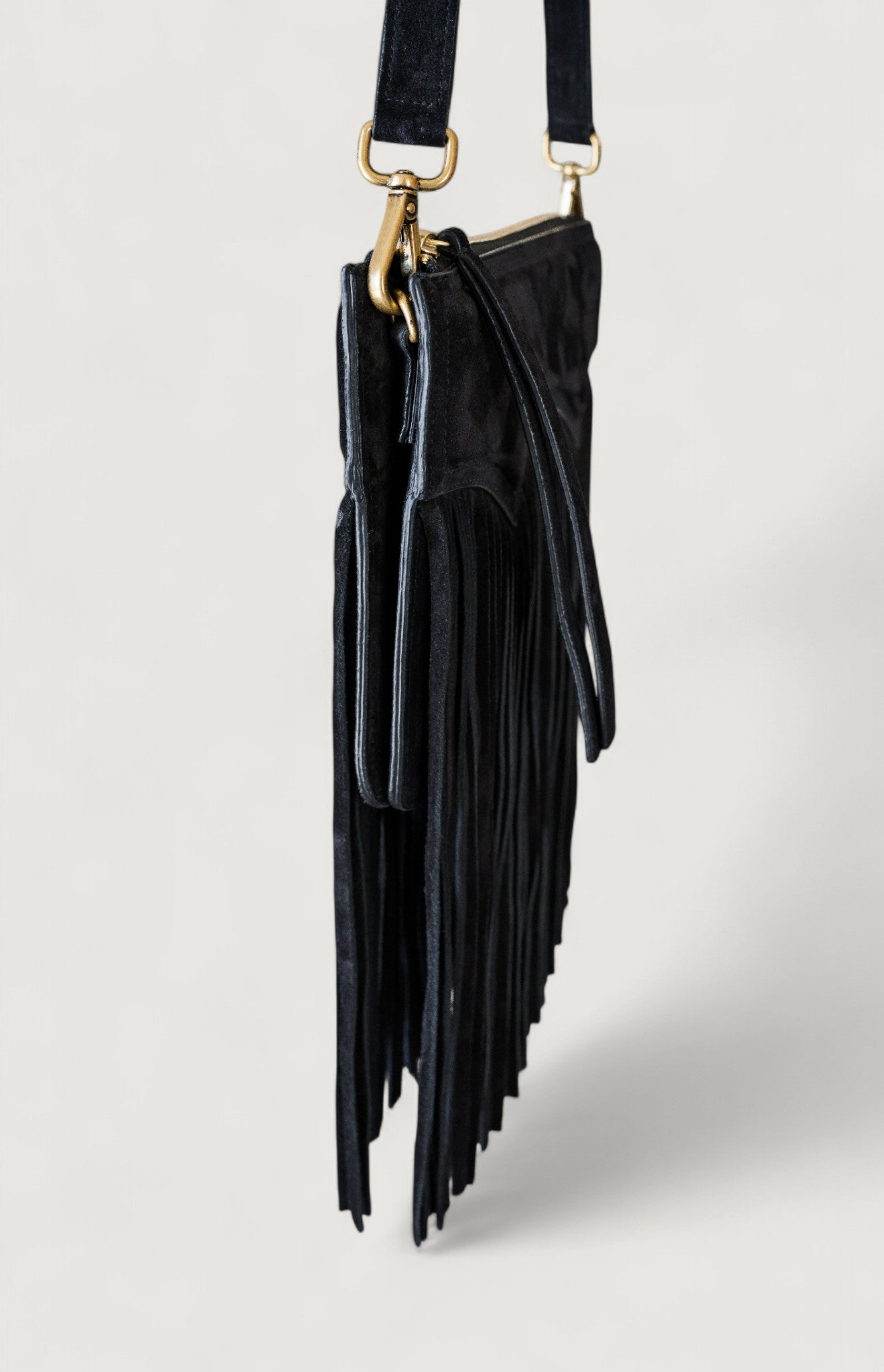 Black fringe handbag with brass hardware on a light gray background