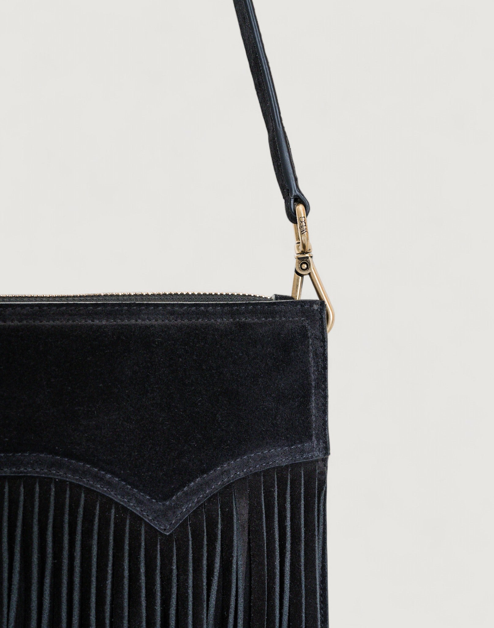 Black suede handbag with fringe detail on a light gray background