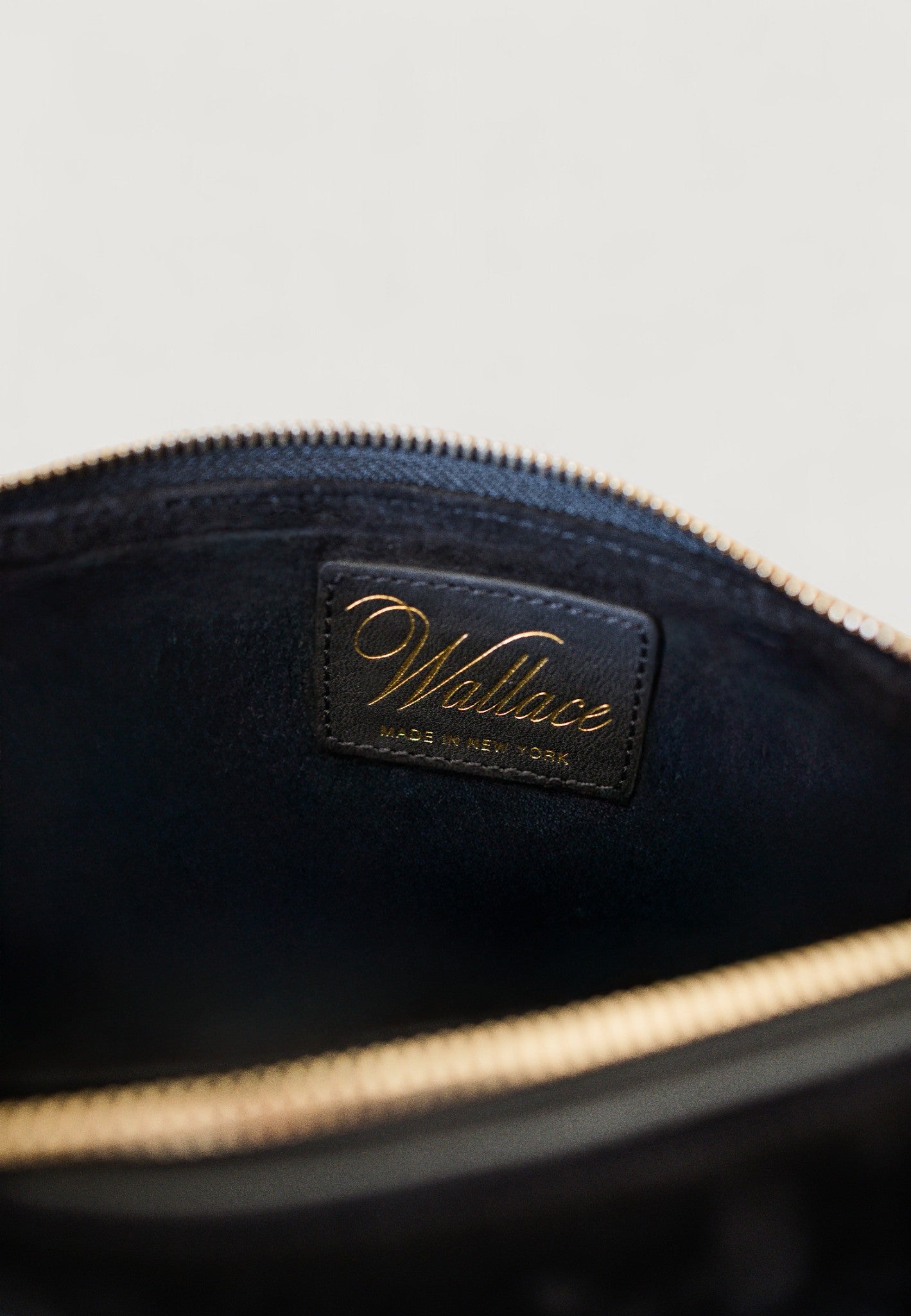 Close-up of a black leather bag with 'Wallace' branding on a light gray background