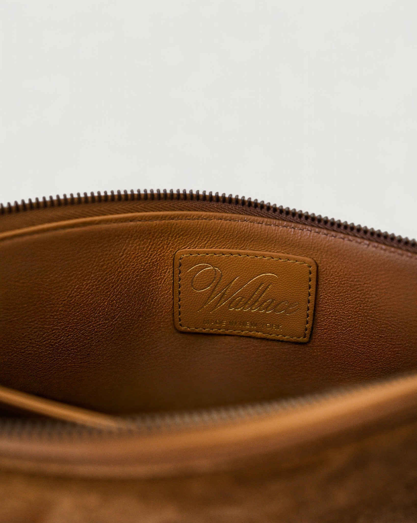 Close-up of a brown leather pouch with a visible brand label on a light gray background