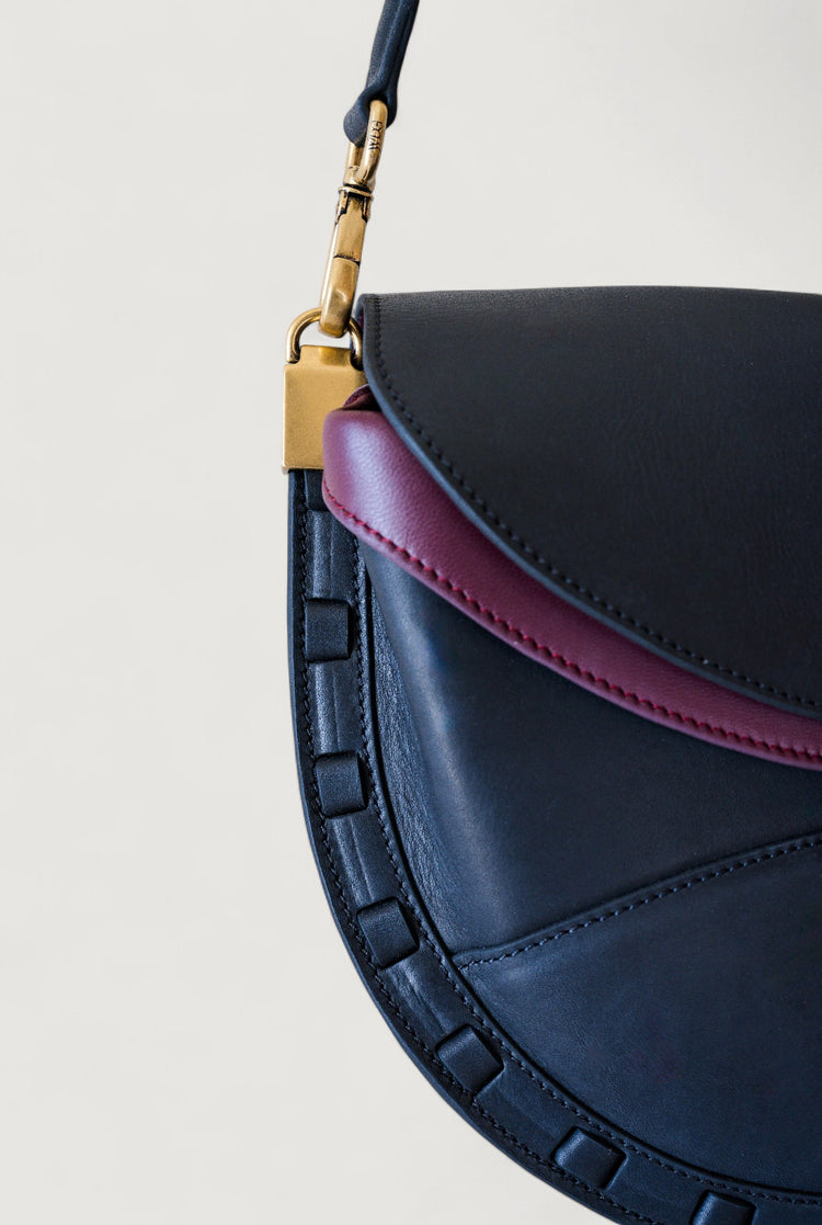 Black and burgundy handbag with brass clasp on a light gray background