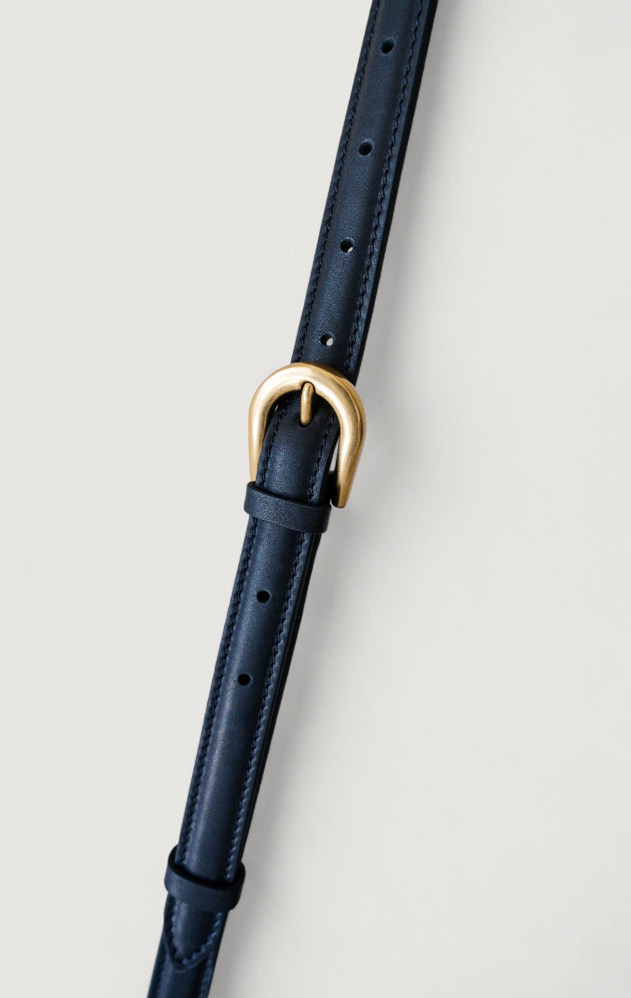 Black leather strap with a brass buckle on a light gray background