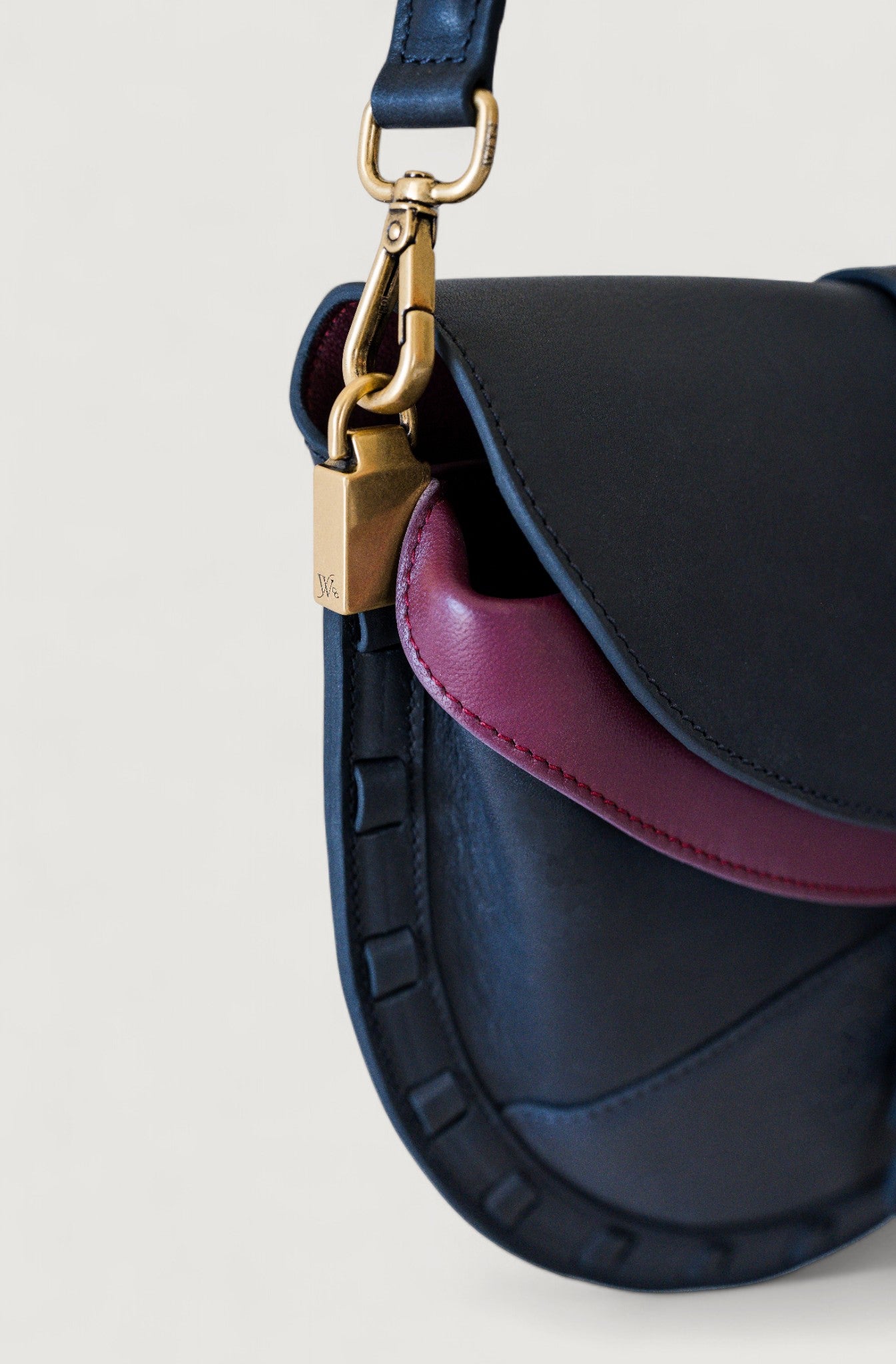 Black and burgundy handbag with brass clasp on a light gray background