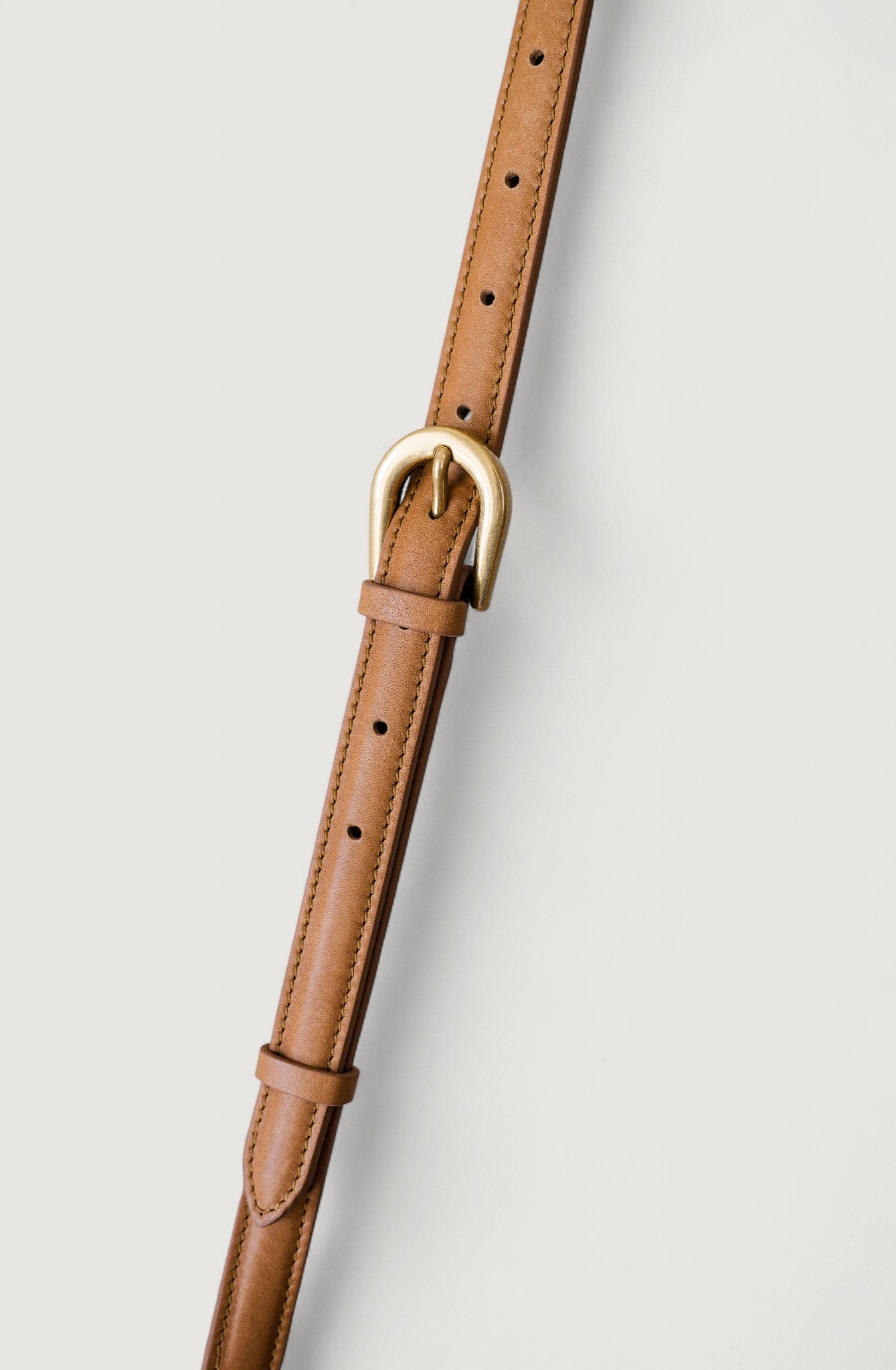 Brown leather shoulder strap with a brass buckle on a light gray background
