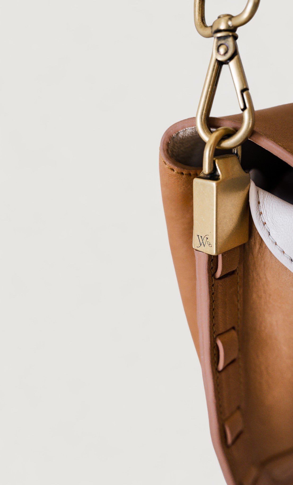 Close-up of a brown leather handbag with a brass buckle on a light gray background