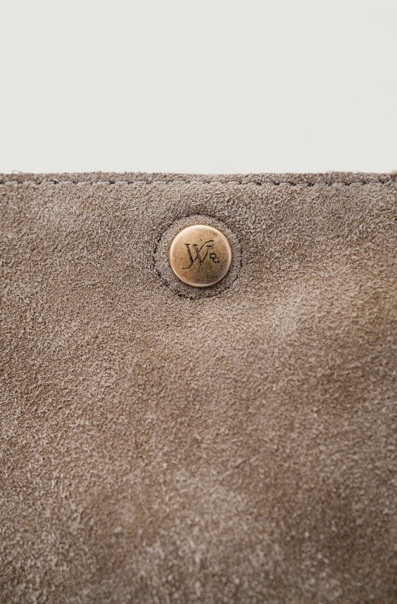 Close-up of a gray suede surface with a metal button featuring a logo.