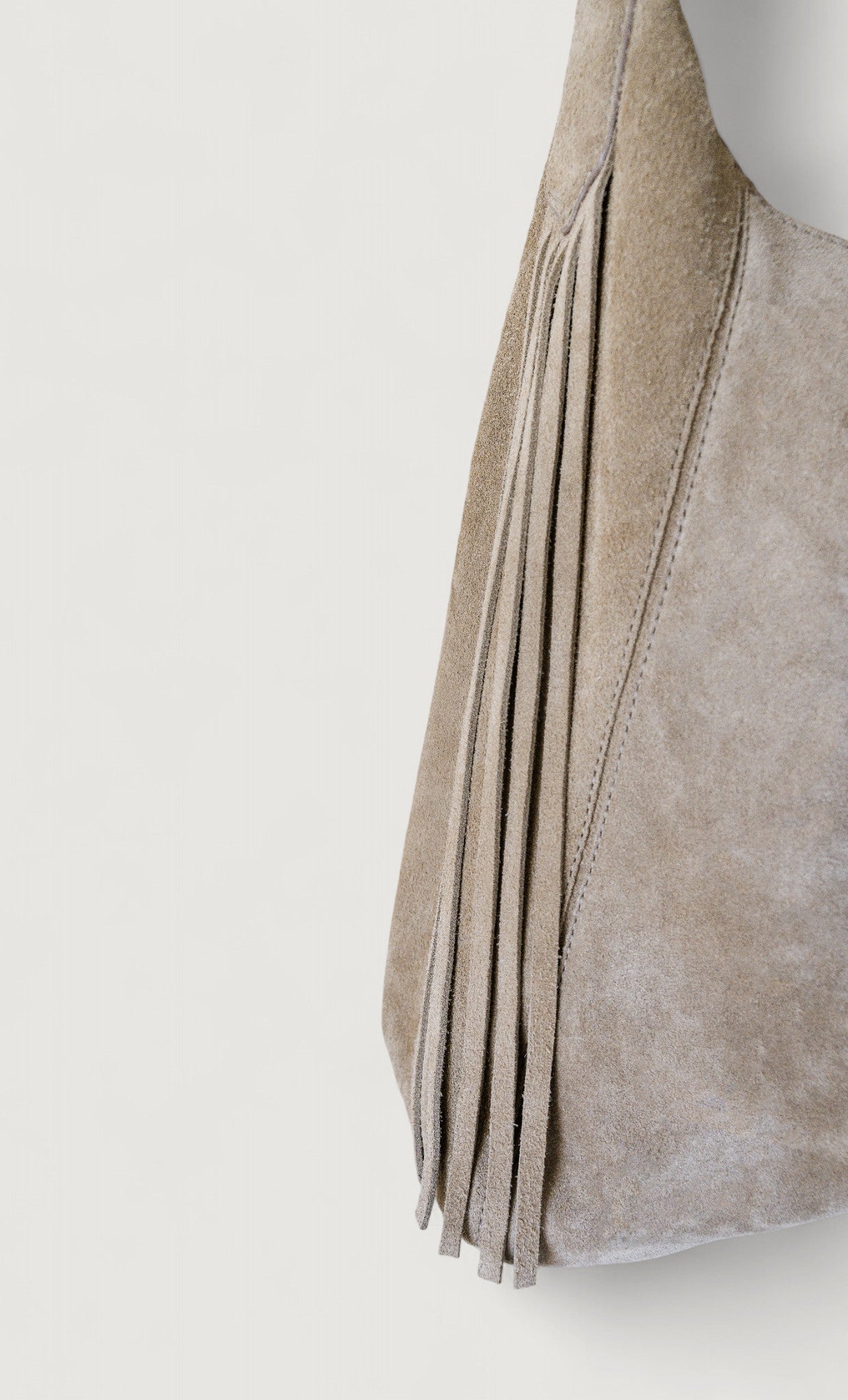 Gray suede handbag with fringe details on a white background