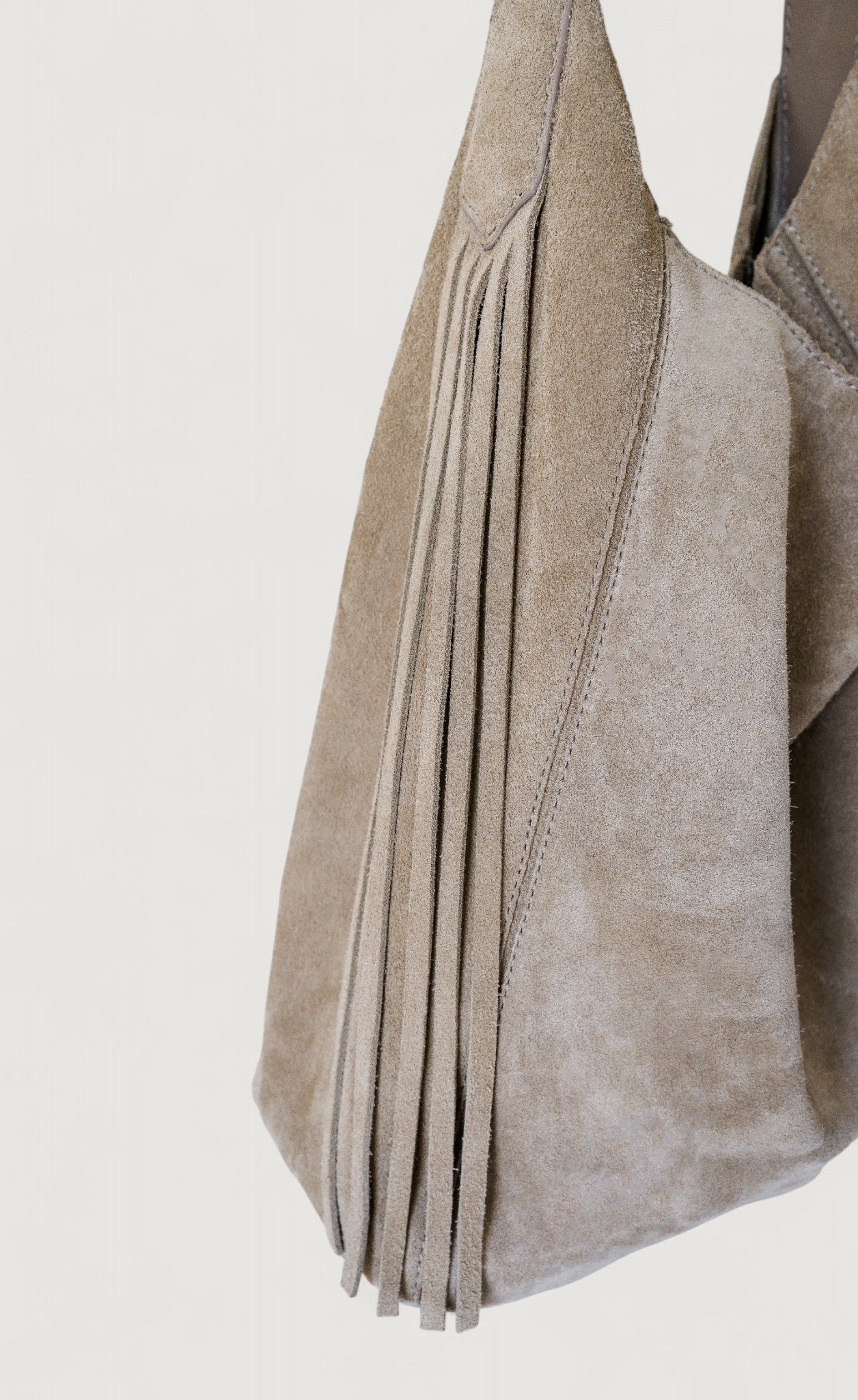 Close-up of a gray suede handbag with pleated design on a light gray background