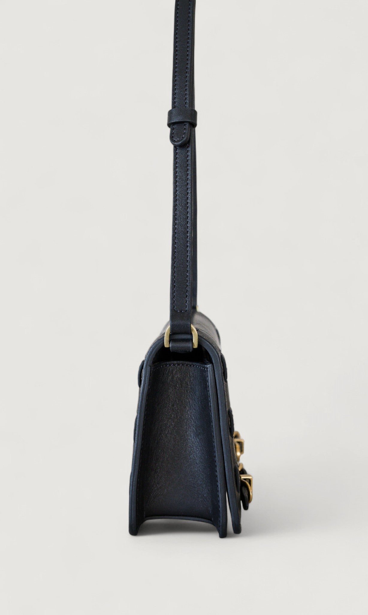 Black handbag with brass accents on a light gray background