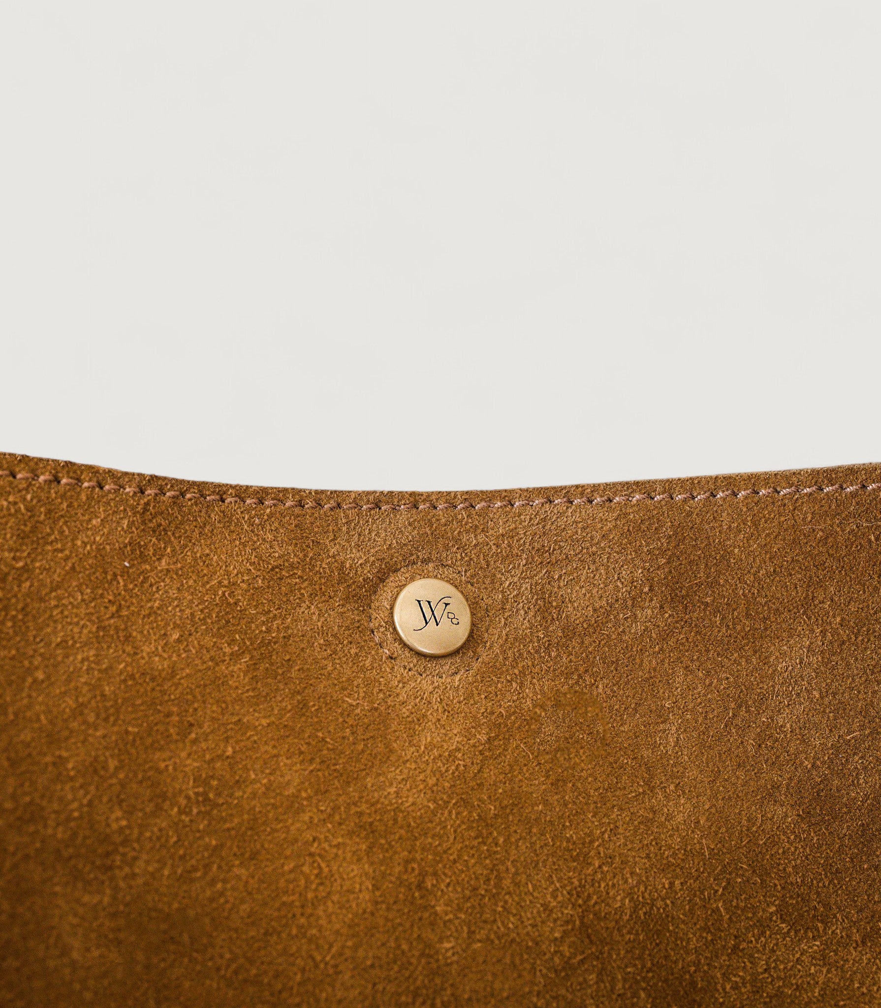 Close-up of a brown leather product with a brass logo on a light gray background