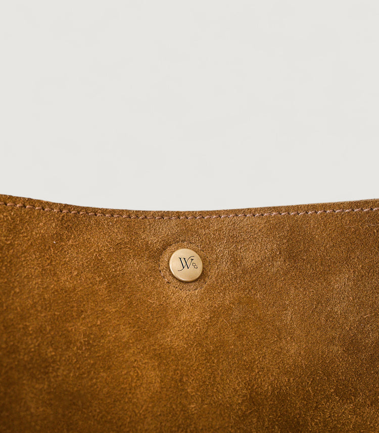 Close-up of a brown leather product with a brass logo on a light gray background