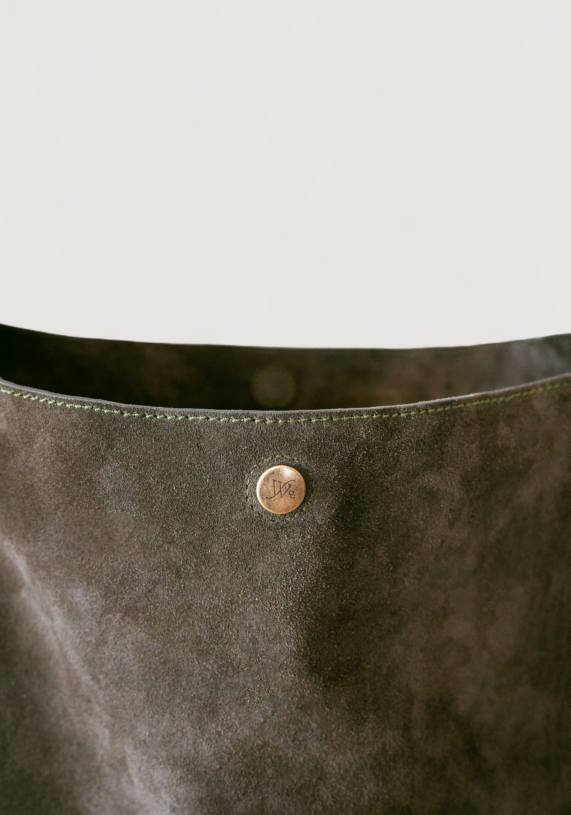 Close-up of an olive color leather bag with a brass button on a light gray background