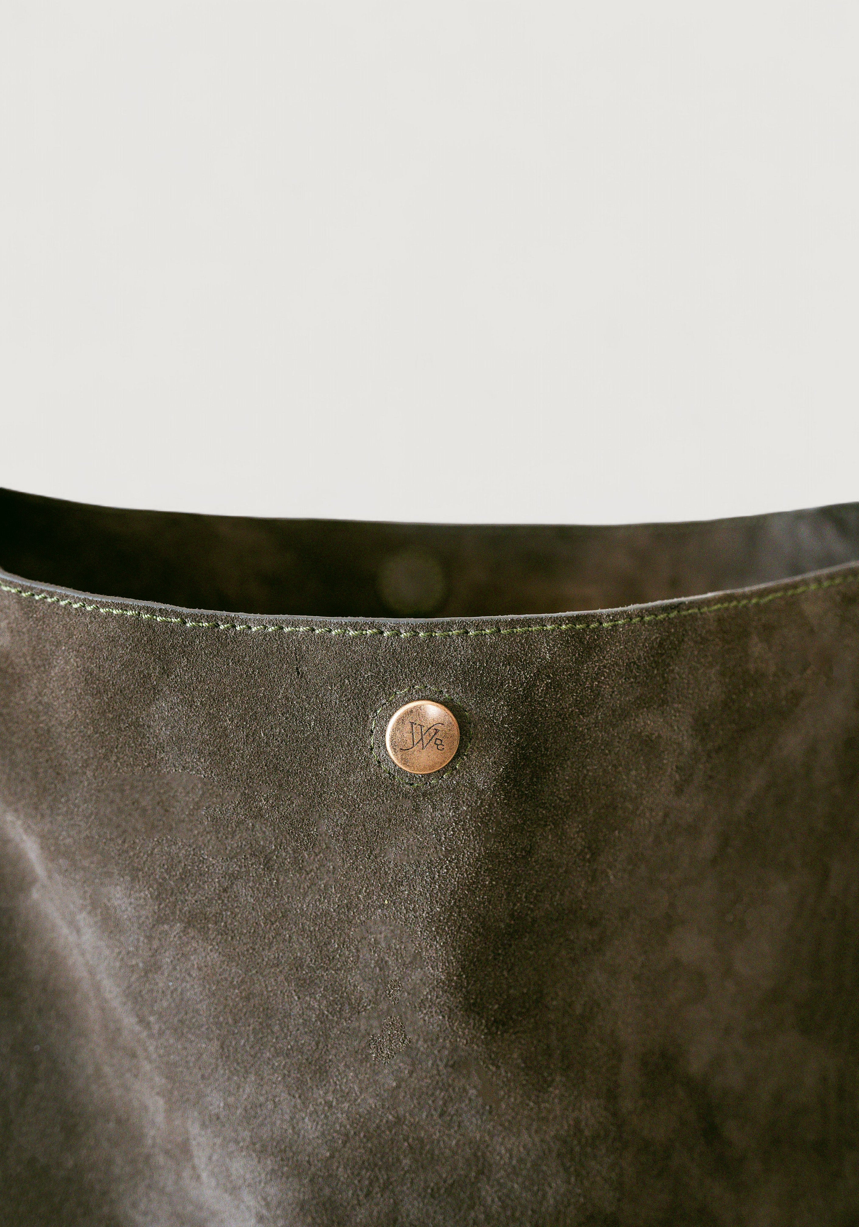 Close-up of an olive color leather bag with a brass button on a light gray background