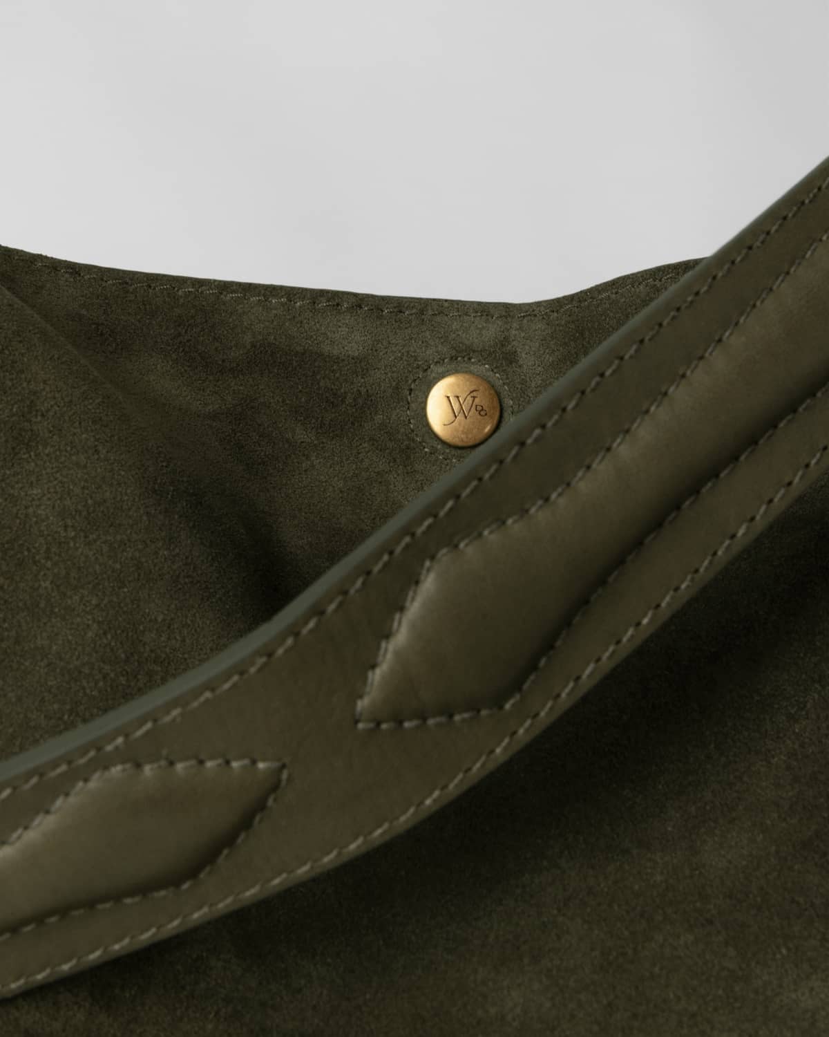 Close-up of a olive color leather bag with a brass button on a light gray background