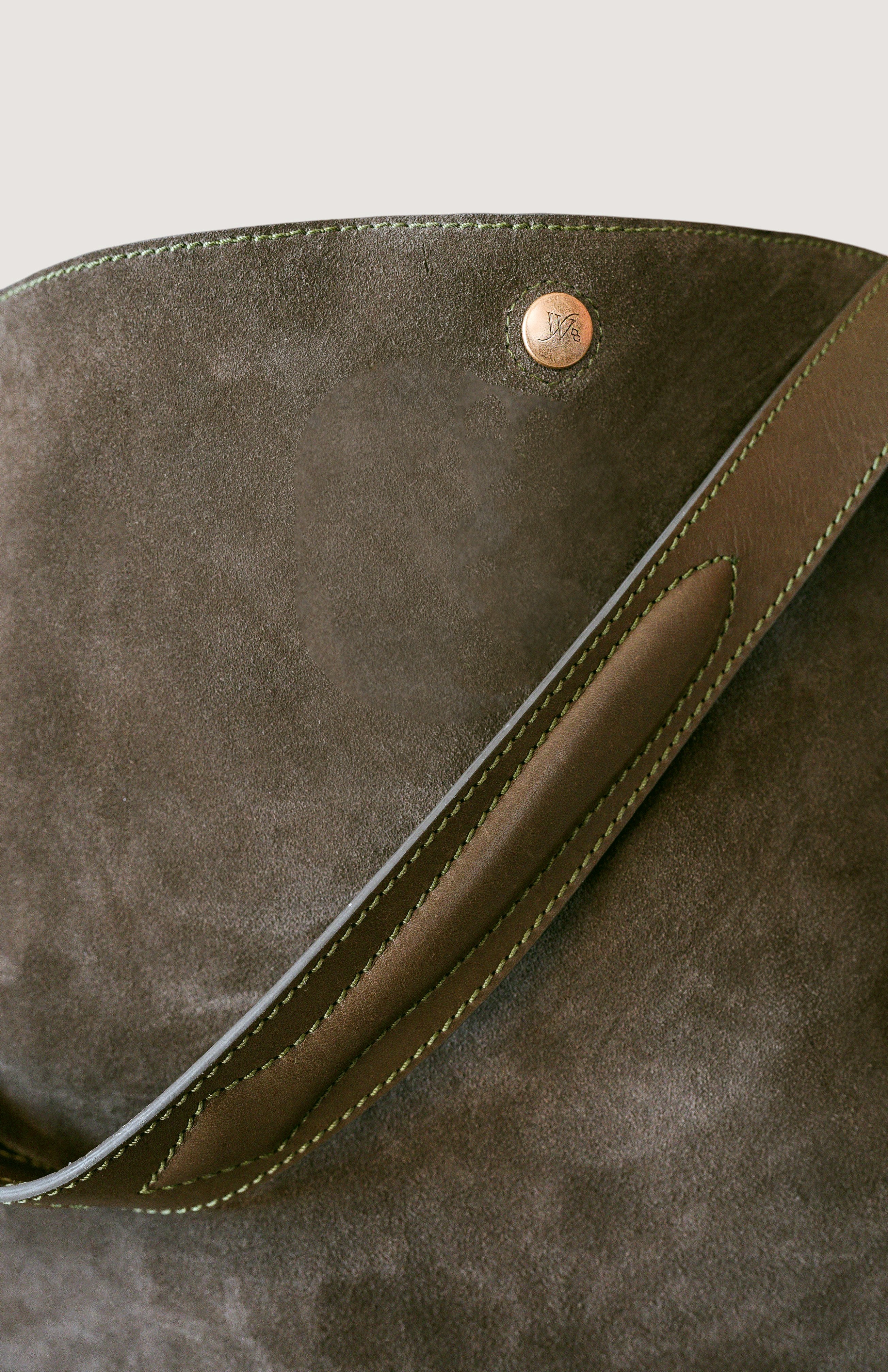 Close-up of a olive color leather bag with a brass button on a light gray background