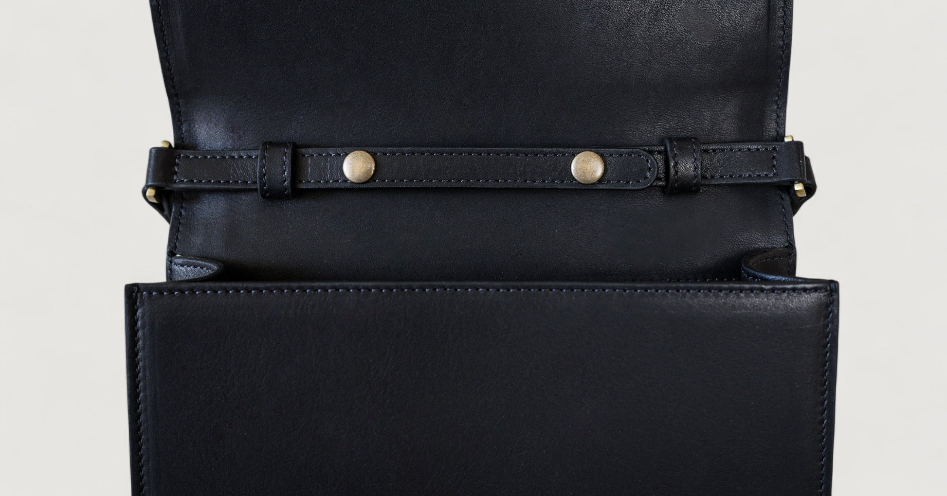 Close-up of a black leather bag with gold hardware on a light gray background