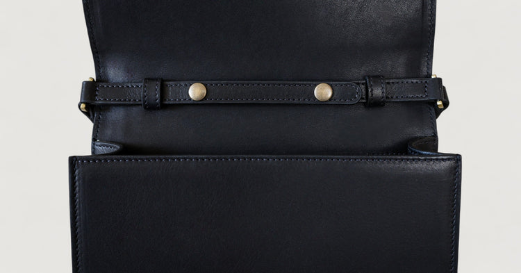 Close-up of a black leather bag with gold hardware on a light gray background
