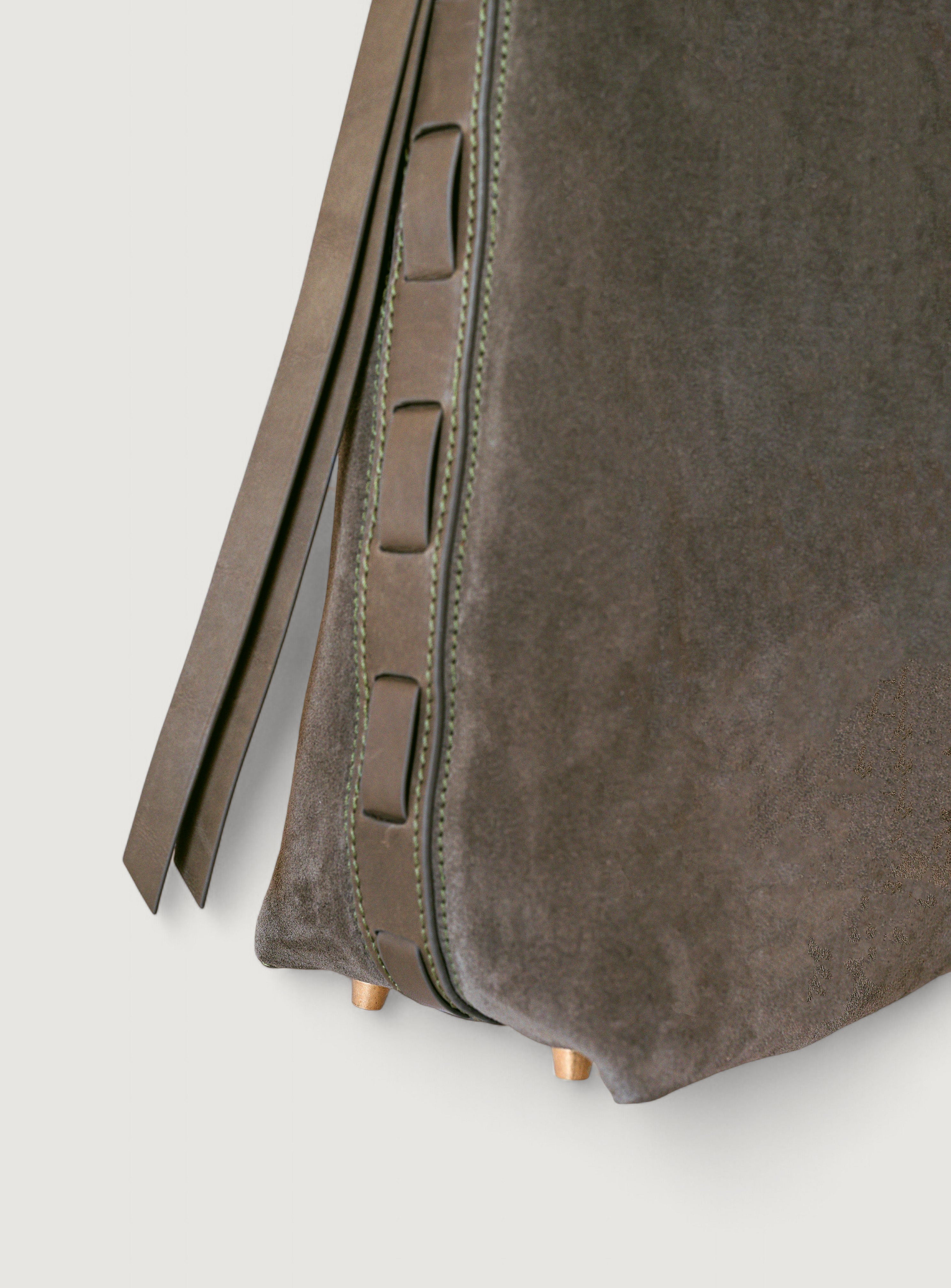 Close-up of a olive color suede bag with a strap on a light gray background