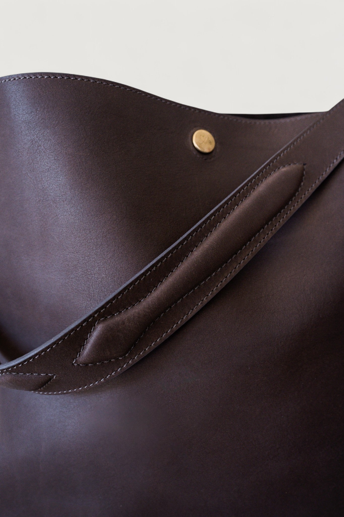 Close-up of a brown leather bag with a brass button on a light gray background