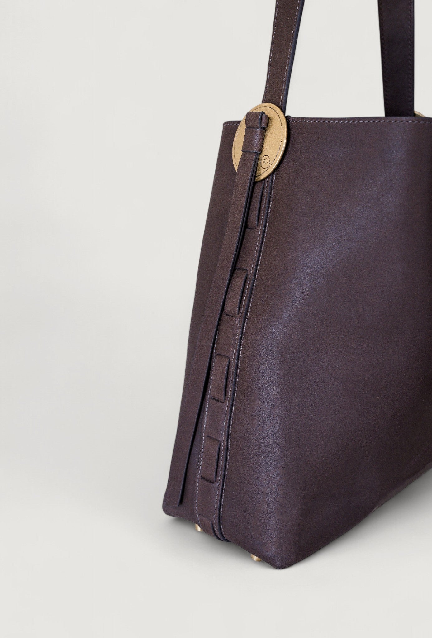 Brown leather handbag with a brass concho on a light gray background