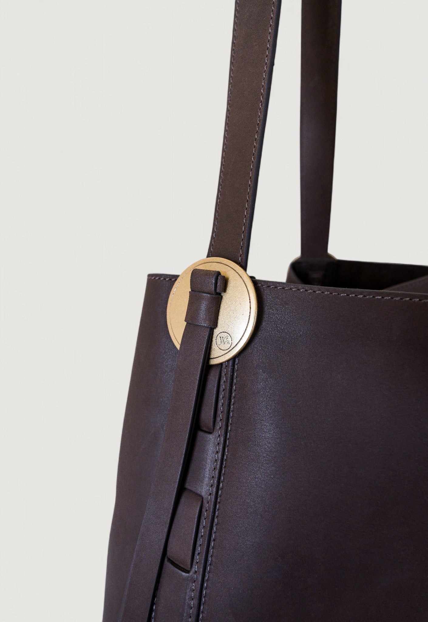 Brown leather tote bag with a brass concho on a light gray background
